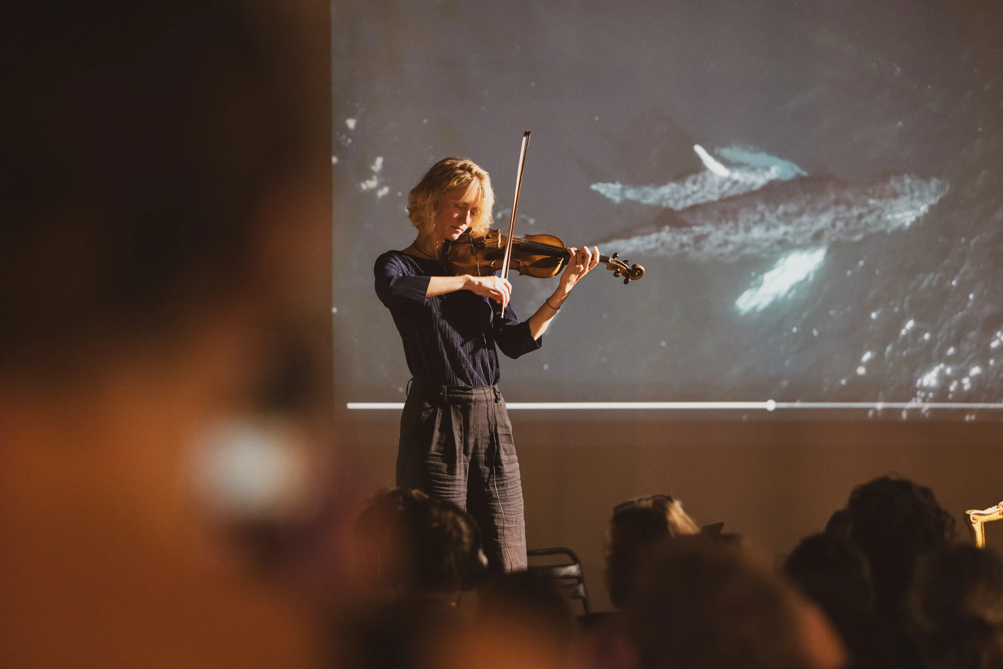 Marie-Kell playing violin on stage in front of a projection of a whale